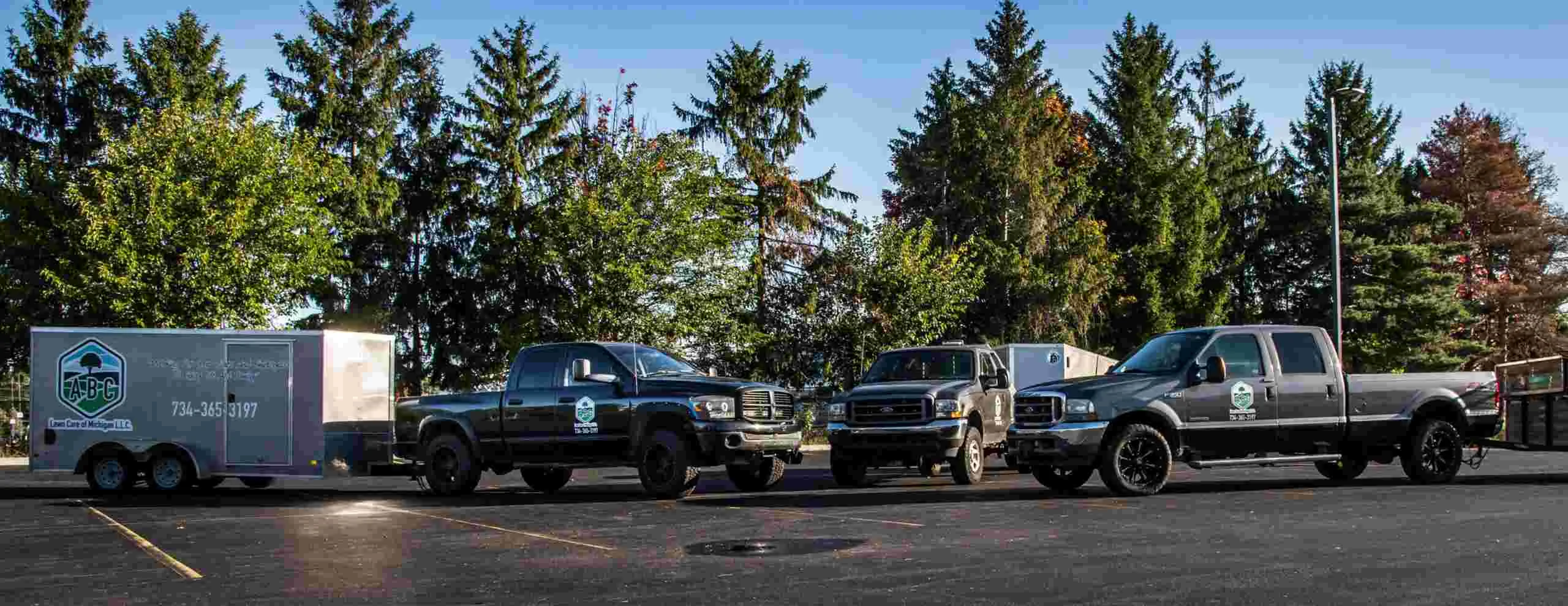 ABC Lawn Care of Michigan trucks and branded trailer lined up in New Boston